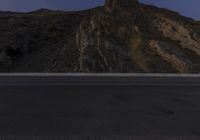 a lone skateboarder makes his way down the highway past some mountains and steep cliffs