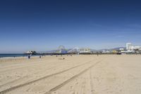 people walk on sand at a beach, near the ocean in the distance is a sky with few cloudless, and blue skies