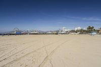 people walk on sand at a beach, near the ocean in the distance is a sky with few cloudless, and blue skies