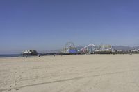 people walk on sand at a beach, near the ocean in the distance is a sky with few cloudless, and blue skies