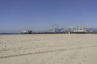 people walk on sand at a beach, near the ocean in the distance is a sky with few cloudless, and blue skies