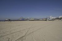 people walk on sand at a beach, near the ocean in the distance is a sky with few cloudless, and blue skies