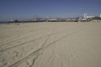 people walk on sand at a beach, near the ocean in the distance is a sky with few cloudless, and blue skies