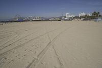 people walk on sand at a beach, near the ocean in the distance is a sky with few cloudless, and blue skies