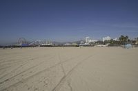 people walk on sand at a beach, near the ocean in the distance is a sky with few cloudless, and blue skies