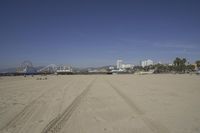 people walk on sand at a beach, near the ocean in the distance is a sky with few cloudless, and blue skies