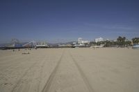 people walk on sand at a beach, near the ocean in the distance is a sky with few cloudless, and blue skies