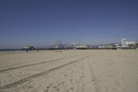 people walk on sand at a beach, near the ocean in the distance is a sky with few cloudless, and blue skies