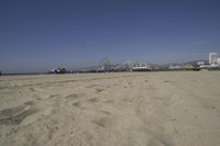 people walk on sand at a beach, near the ocean in the distance is a sky with few cloudless, and blue skies