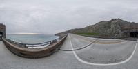 an image of a road and a cliff by the ocean at dawn from a fisheye lens