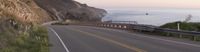 a paved road with a large cliff next to the ocean with boats on it at dusk