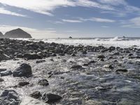 an ocean and rocks coast with some surfers in the water with blue skies in background