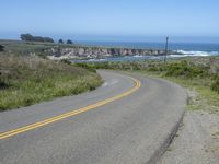 an empty road on a hill overlooking the ocean and a rocky coastline in the distance