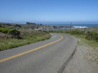 an empty road on a hill overlooking the ocean and a rocky coastline in the distance