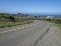 an empty road on a hill overlooking the ocean and a rocky coastline in the distance