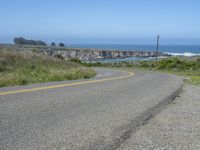 an empty road on a hill overlooking the ocean and a rocky coastline in the distance