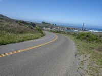 an empty road on a hill overlooking the ocean and a rocky coastline in the distance