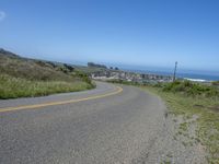 an empty road on a hill overlooking the ocean and a rocky coastline in the distance