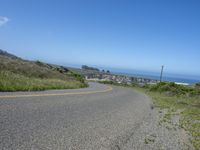 an empty road on a hill overlooking the ocean and a rocky coastline in the distance