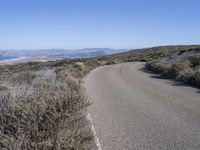 a lone curve of road with mountains and sea in background at the far end of the street