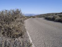 a lone curve of road with mountains and sea in background at the far end of the street