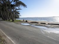 the people are walking on the shore by the road next to the water and sand