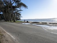 the people are walking on the shore by the road next to the water and sand