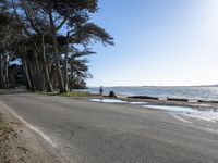 the people are walking on the shore by the road next to the water and sand