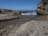 rocky shoreline next to beach with large rock formation in the foreground and a blue sky overhead