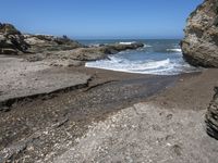 rocky shoreline next to beach with large rock formation in the foreground and a blue sky overhead