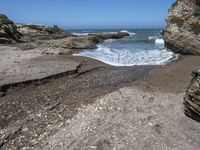 rocky shoreline next to beach with large rock formation in the foreground and a blue sky overhead