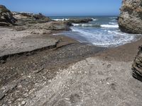 rocky shoreline next to beach with large rock formation in the foreground and a blue sky overhead