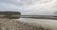 a rocky shore is full of rocks and water near the shoreline with a steep hill in the background