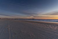 the footprints in the sand at the beach are in the foreground, as the sun sets over a pier