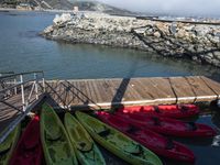 several colorful kayaks are lined up at the dock in the water next to some rocks