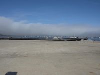 some logs near the water on a shore line with the fog in the background and a few boats docked on shore