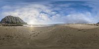 a fisheye lens image of a sandy beach with sand and rocks in the foreground and ocean at low tide