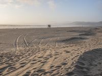 a boat parked on the shore with tracks in the sand and trees and hills in the background