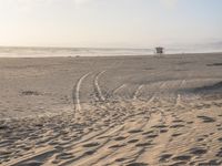 a boat parked on the shore with tracks in the sand and trees and hills in the background