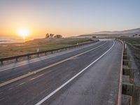 a paved road winds up to the sun as it sets over the ocean in a beautiful landscape