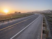 a paved road winds up to the sun as it sets over the ocean in a beautiful landscape