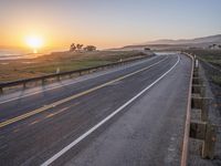 a paved road winds up to the sun as it sets over the ocean in a beautiful landscape