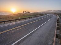 a paved road winds up to the sun as it sets over the ocean in a beautiful landscape