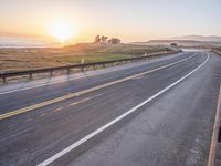 a paved road winds up to the sun as it sets over the ocean in a beautiful landscape