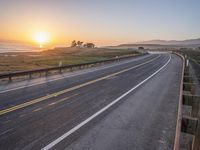 a paved road winds up to the sun as it sets over the ocean in a beautiful landscape