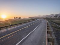 a paved road winds up to the sun as it sets over the ocean in a beautiful landscape