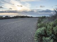 an empty roadway going down to the sea during sunrise or sunset hours in a remote location