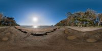 fish eye lens in view of the ocean and land at dusk or sunrise with boats floating near and people on the beach at the shoreline