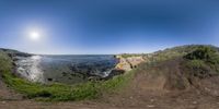 a 360 - view photo of the ocean next to a cliff, showing a bright sun