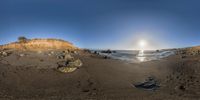 a camera reflection of the sun reflecting over the ocean and some rocks on a beach